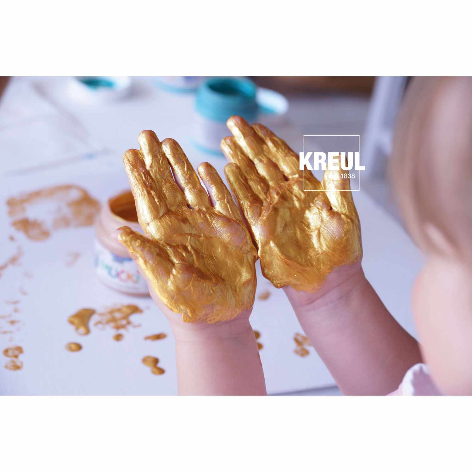 MUCKI Funkel-Fingerfarbe: Kind malt mit goldener Farbe von KREUL. Hände voller leuchtender Farbe.