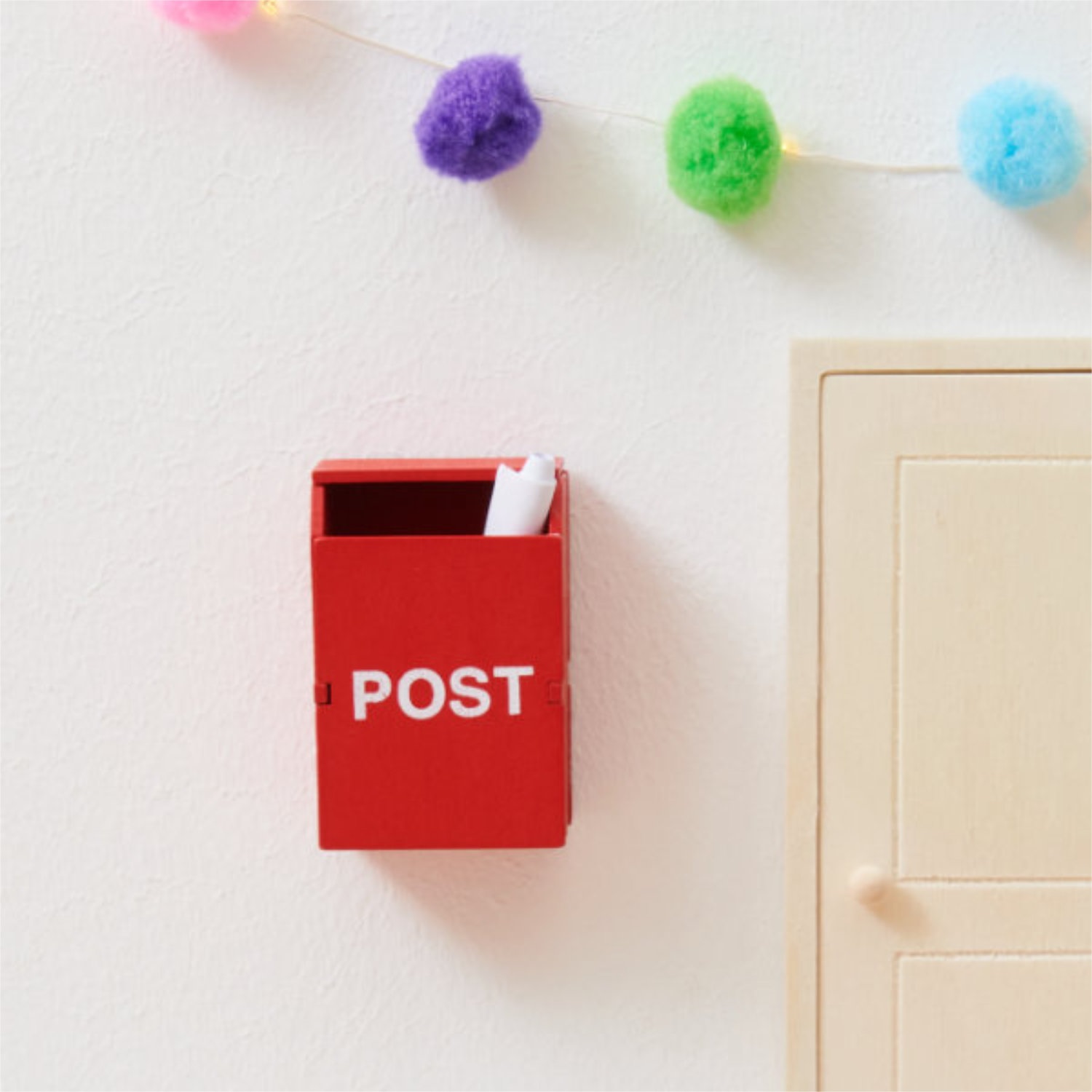 Ein roter Miniatur-Briefkasten mit weißem Papier gefüllt, daneben Ausschnitt einer Holztür.