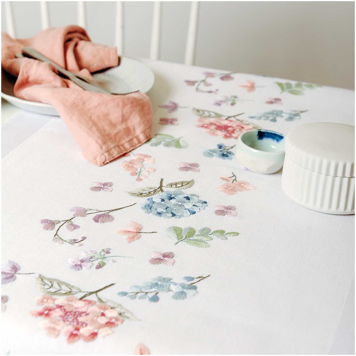 Stickpackung Läufer Hortensien zeigt zarte Blumenstickerei auf weißem Stoff, ideal für elegante Tischdekoration.