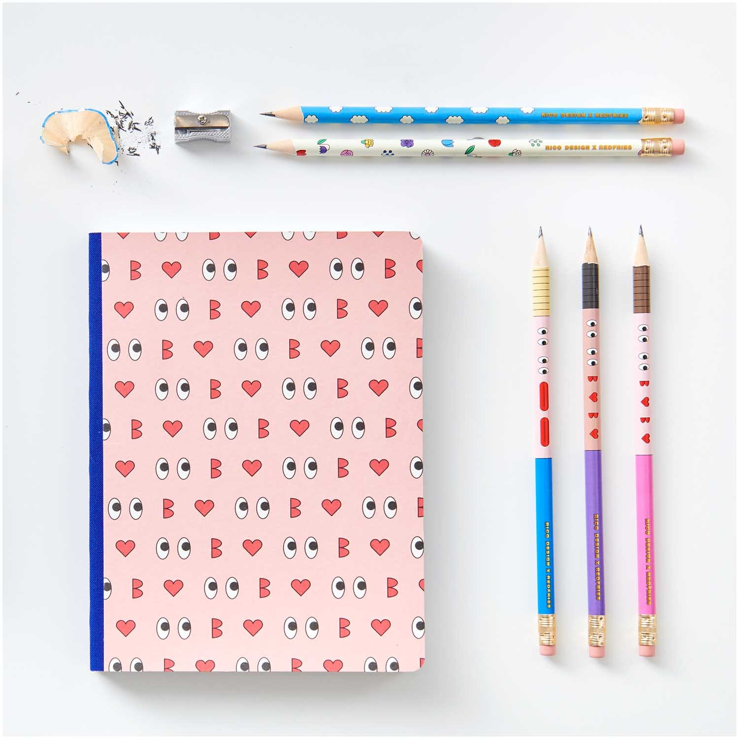 Rico Design x Redfries Bleistifte Eye Candy 5er-Set neben einem Notizbuch mit Augen- und Herzmotiven, umgeben von einem Anspitzer und Radiergummi.