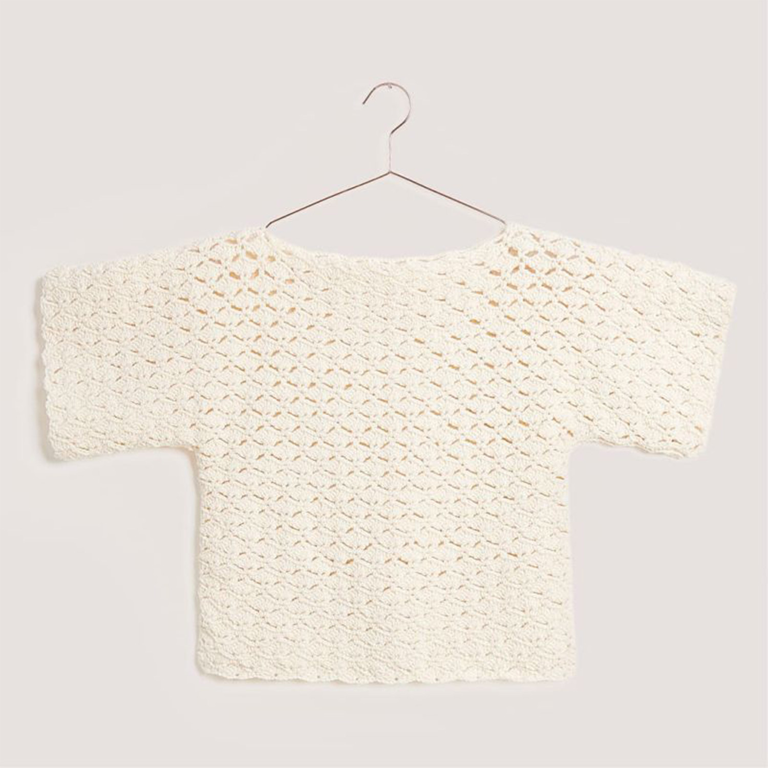 Häkelset Shirt Modell 06 aus Boho Crochet: Ein cremefarbenes, gehäkeltes Shirt auf einem Kleiderbügel.