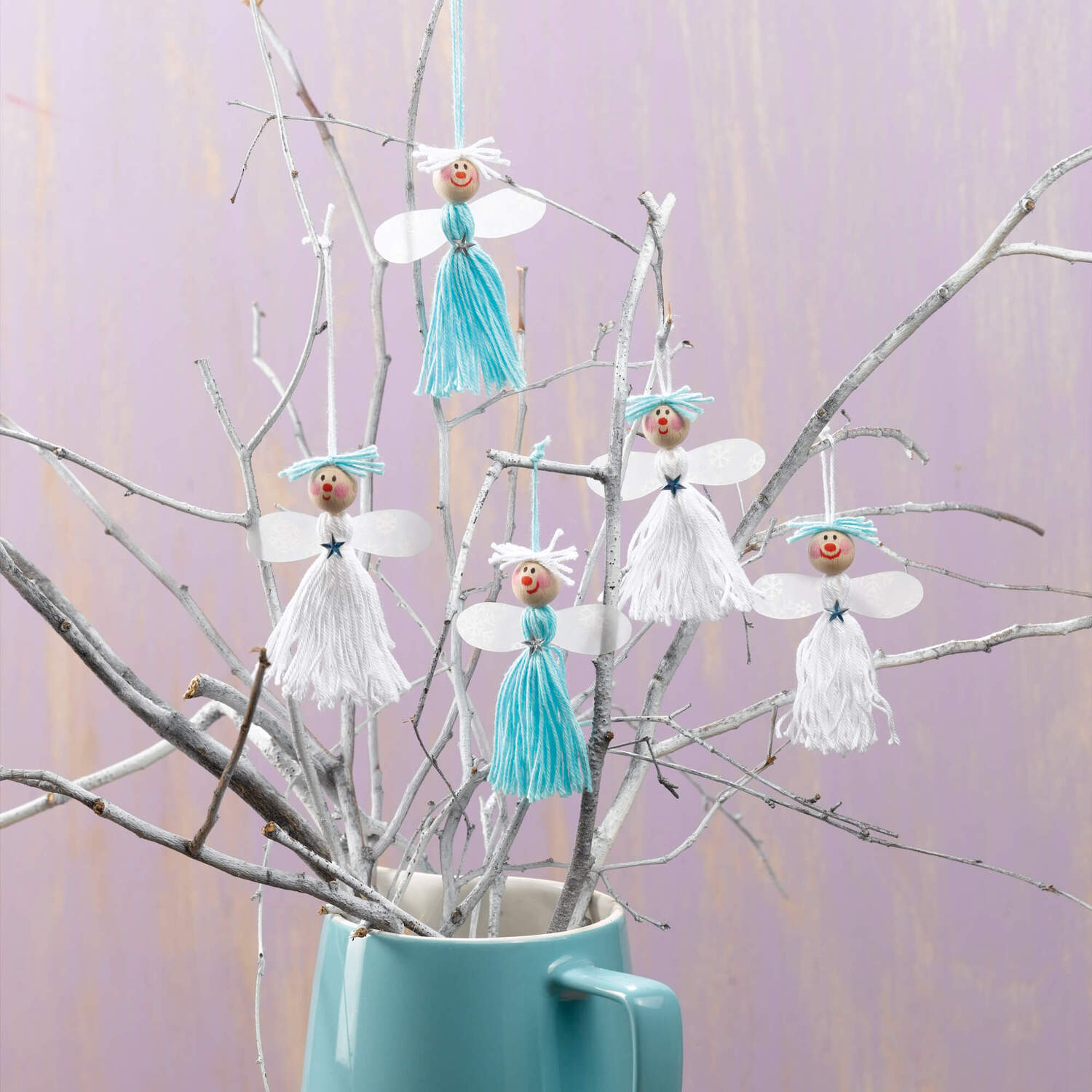 Bastelanleitung Weihnachtsengel: Handgefertigte Engel aus Garn und Holzperlen an Zweigen in einer blauen Vase.