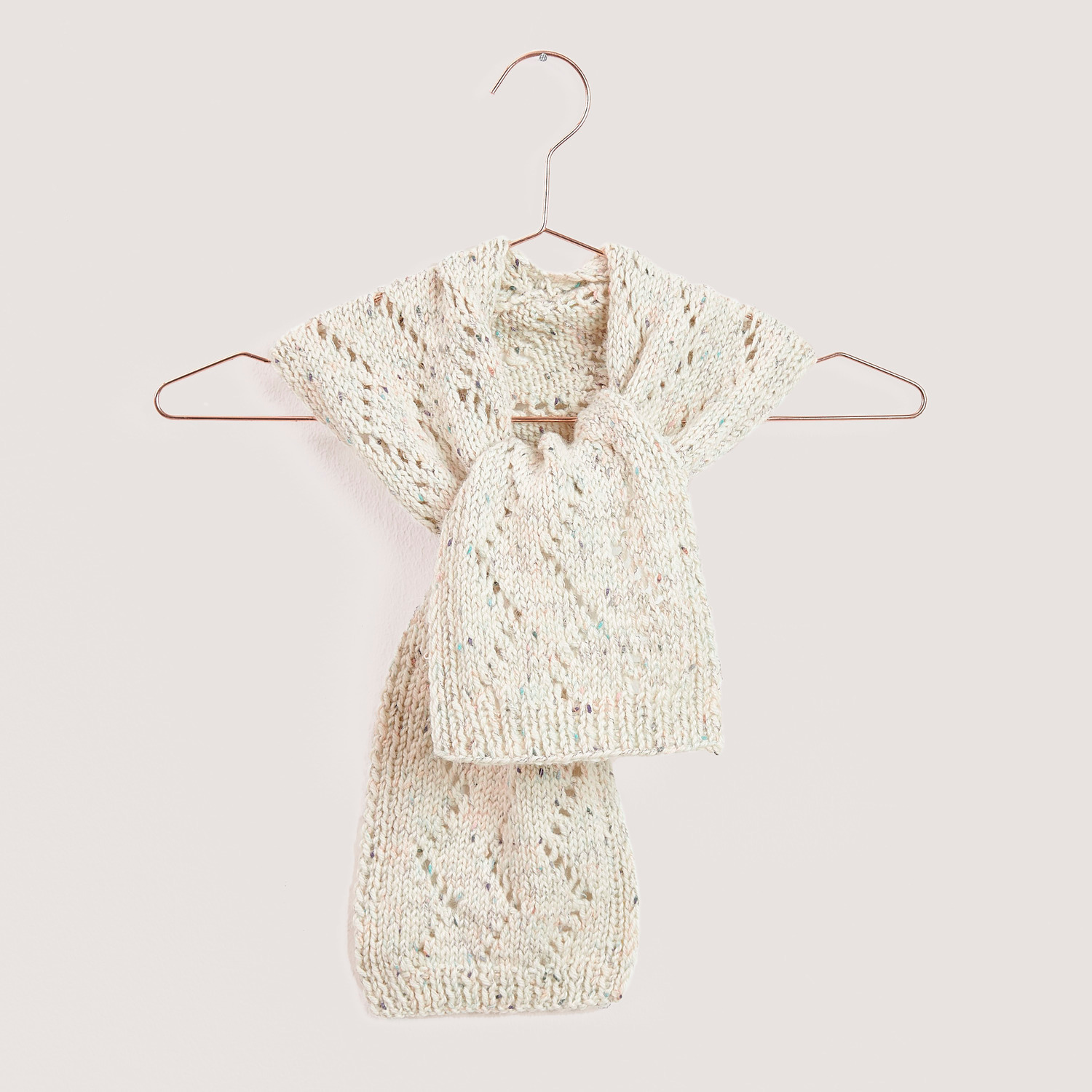 Strickset Mini Tuch Modell 10 von Rico Design, cremefarben, auf einem Kleiderbügel präsentiert.