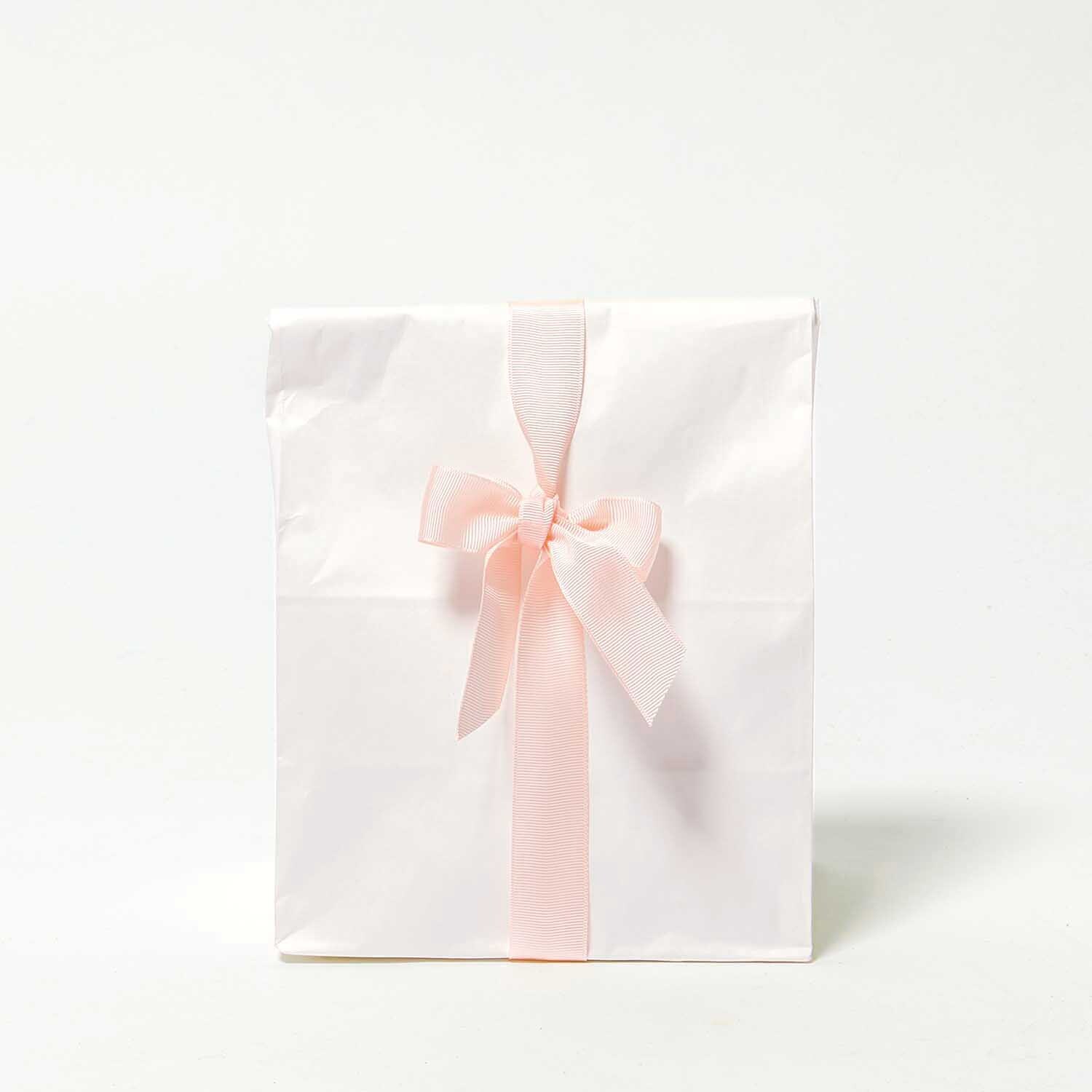 Paper Poetry Ripsband, hellrosa, dekoriert eine weiße Geschenktüte mit einer eleganten Schleife.