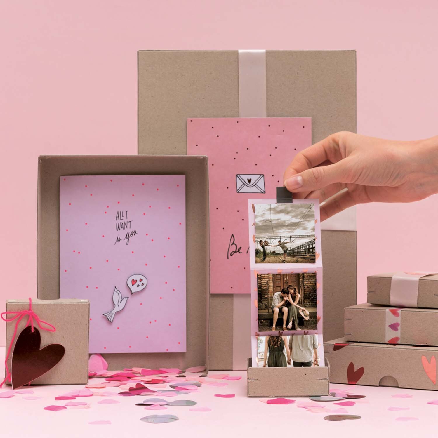 Bastelanleitung Fotobox: Hand zieht Fotos aus einer dekorativen Box mit rosa und braunen Geschenken.