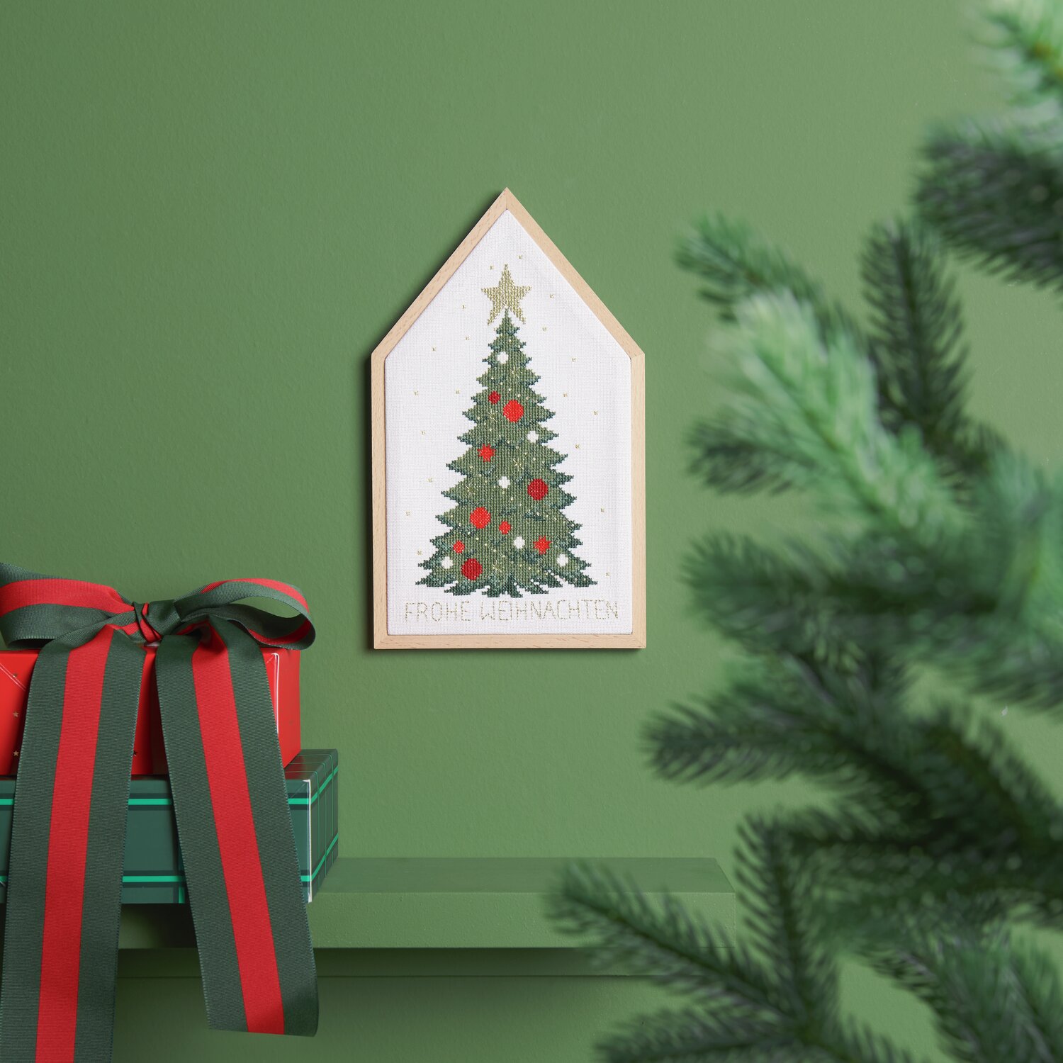 Stickpackung Weihnachtsbaum von Rico Design zeigt einen gestickten Weihnachtsbaum in einem Holzrahmen, dekoriert mit roten Kugeln und einem goldenen Stern.