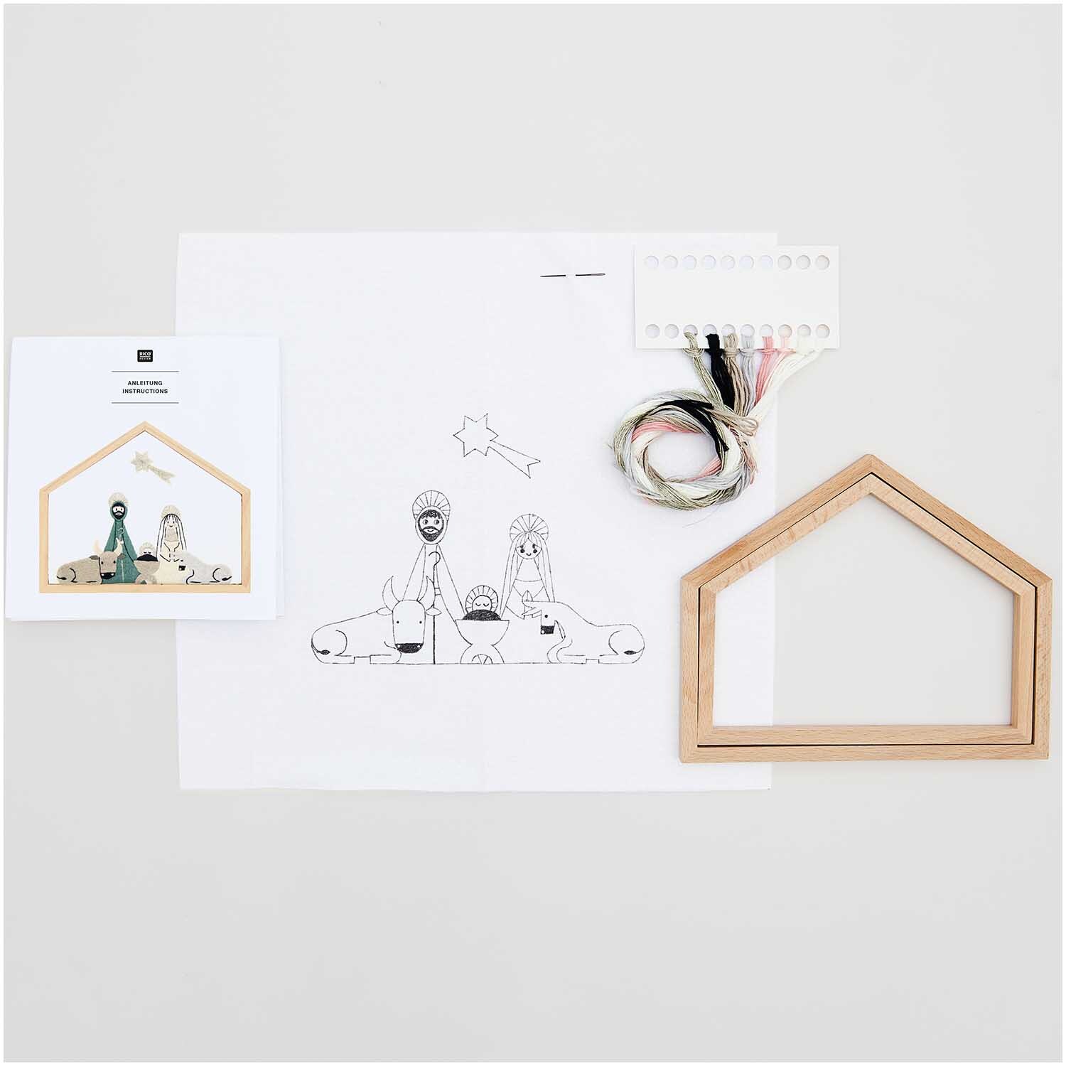 Stickpackung Krippe klein vorgezeichnet 20x16,5cm von Rico Design mit Holzrahmen, Garn und Anleitung auf weißem Hintergrund.