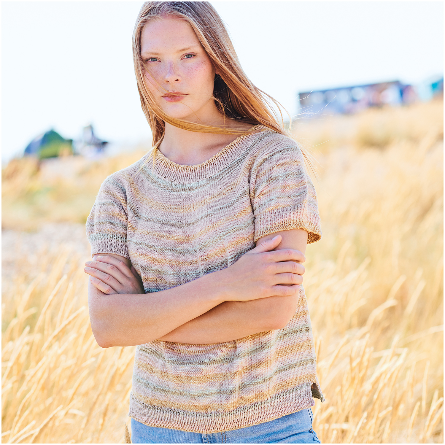 Creative Cotton Camouflage: Frau im gestreiften Strickpullover "Dusty Sunrise" von Rico Design in sommerlicher Landschaft.