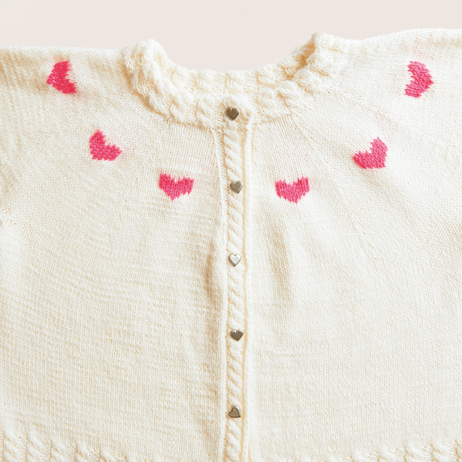 Strickset Cardigan Modell 17 mit Herzknöpfen und neon-pinken Herzmotiven auf cremefarbenem Hintergrund.