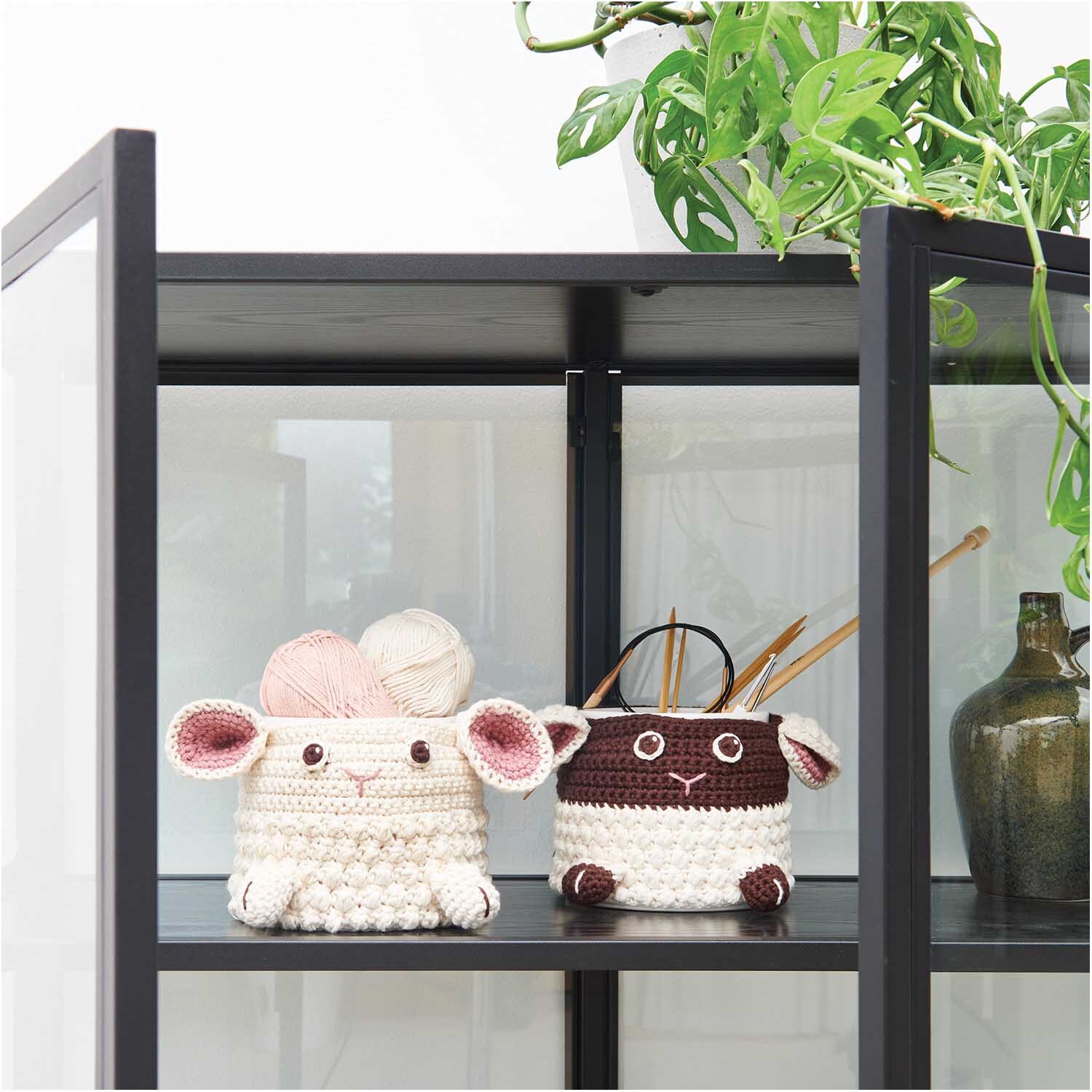 Creative Cotton aran: Zwei gehäkelte Körbe in Tierform auf einem Regal, umgeben von Pflanzen. Ideal für kreative Aufbewahrung.