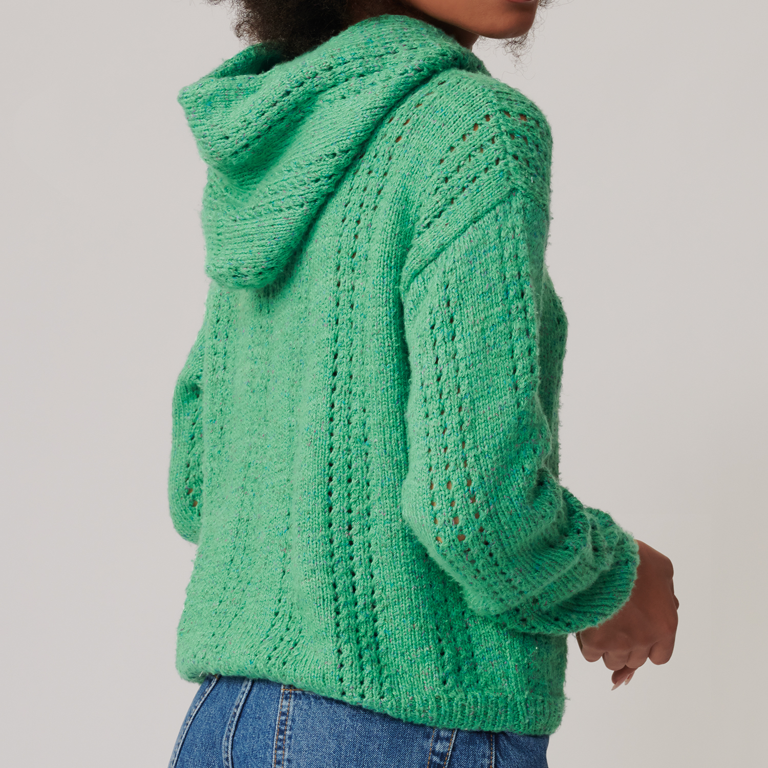 Strickanleitung Hoodie aus Fashion Cottony: Frau trägt grünen, gestrickten Hoodie mit Kapuze, kombiniert mit blauen Jeans.