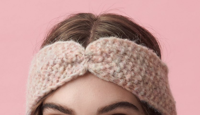 Strickanleitung Stirnband und Dreieckstuch aus Fashion Skinny Alpaca aran. Frau trägt ein gestricktes Stirnband in Pastelltönen vor rosa Hintergrund.