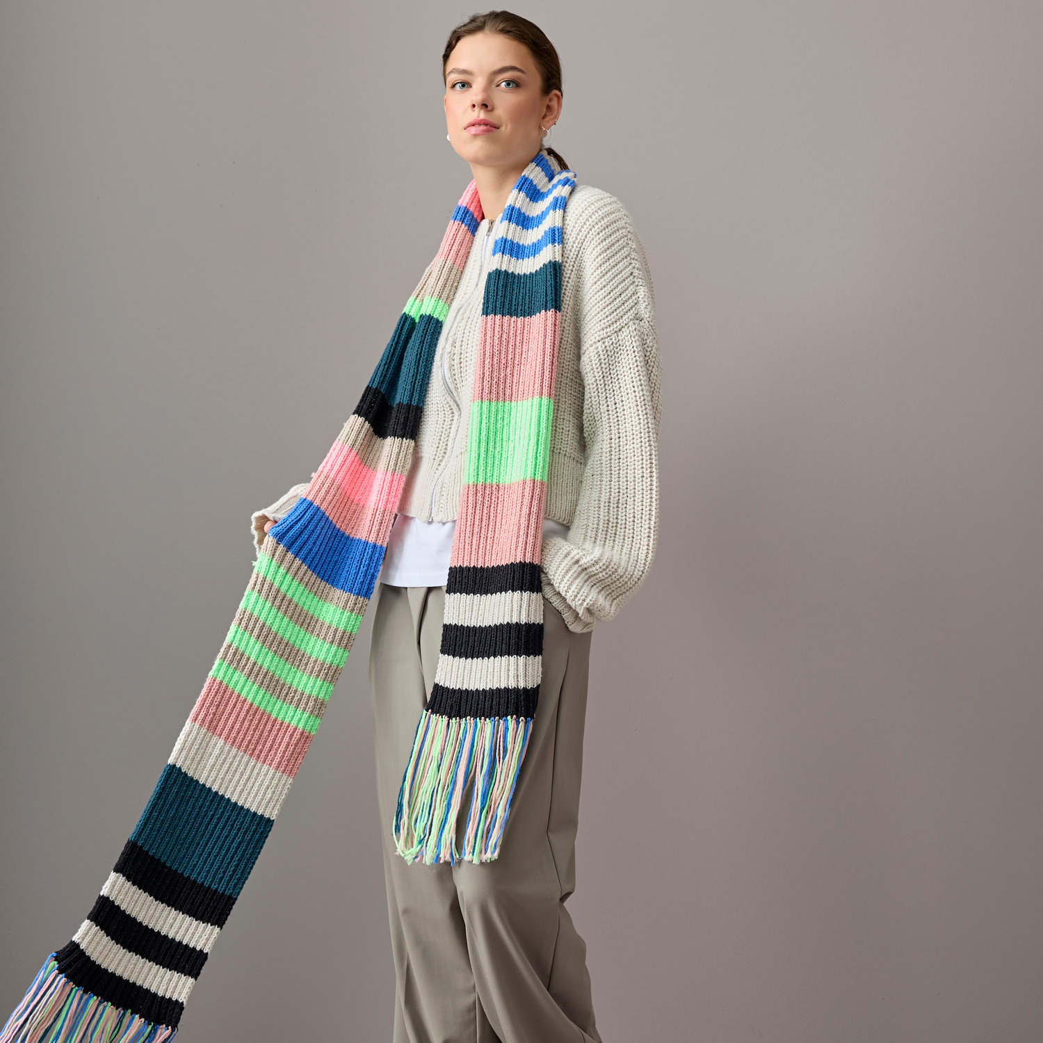 Vegan Cashmere Special: Person trägt langen, gestreiften Schal in Altrosa, Blau, Grün und Creme von Rico Design.