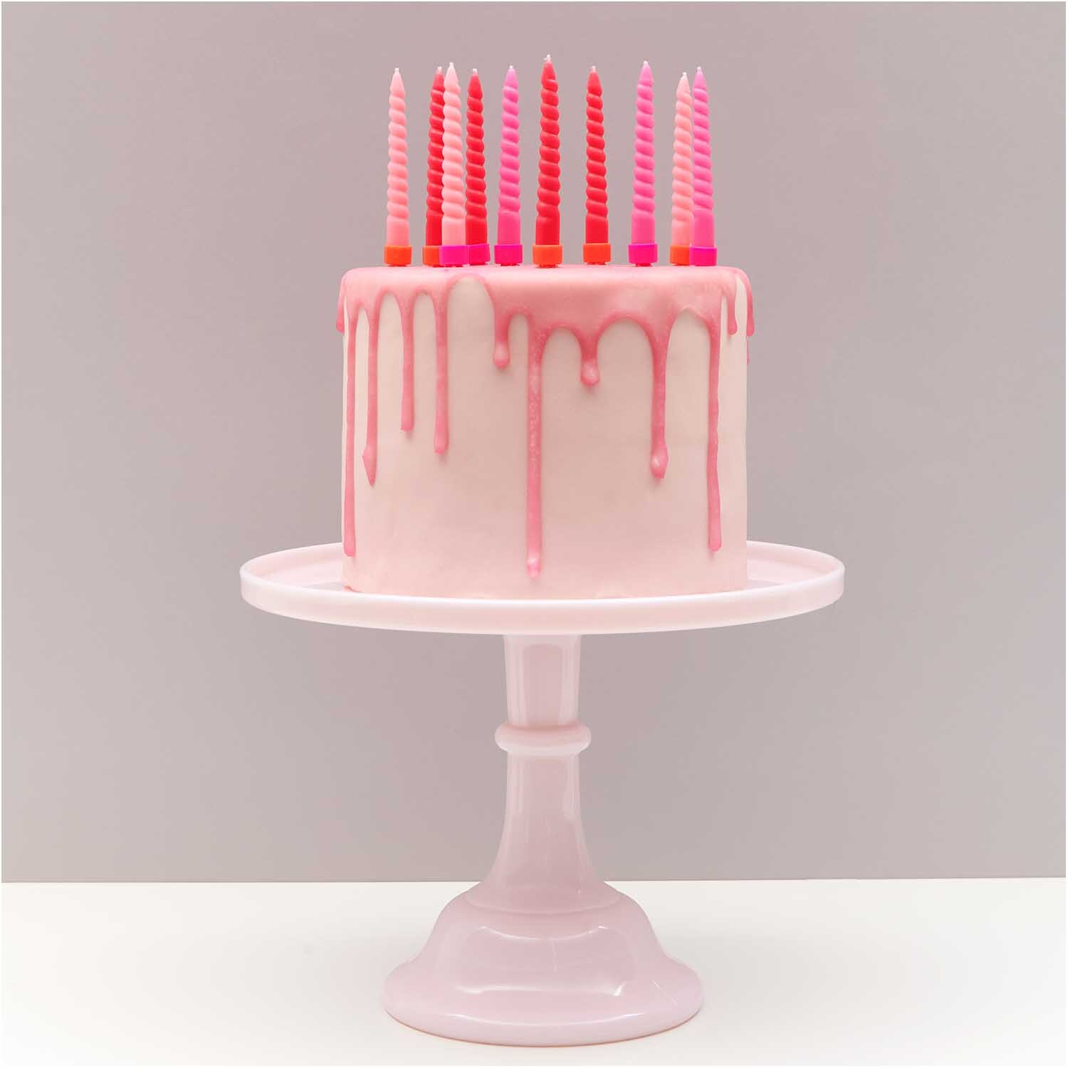 Spiralkerzen pink Mix 1,2x10cm 10 Stück auf rosa Torte mit Tropfglasur auf weißem Kuchenständer.