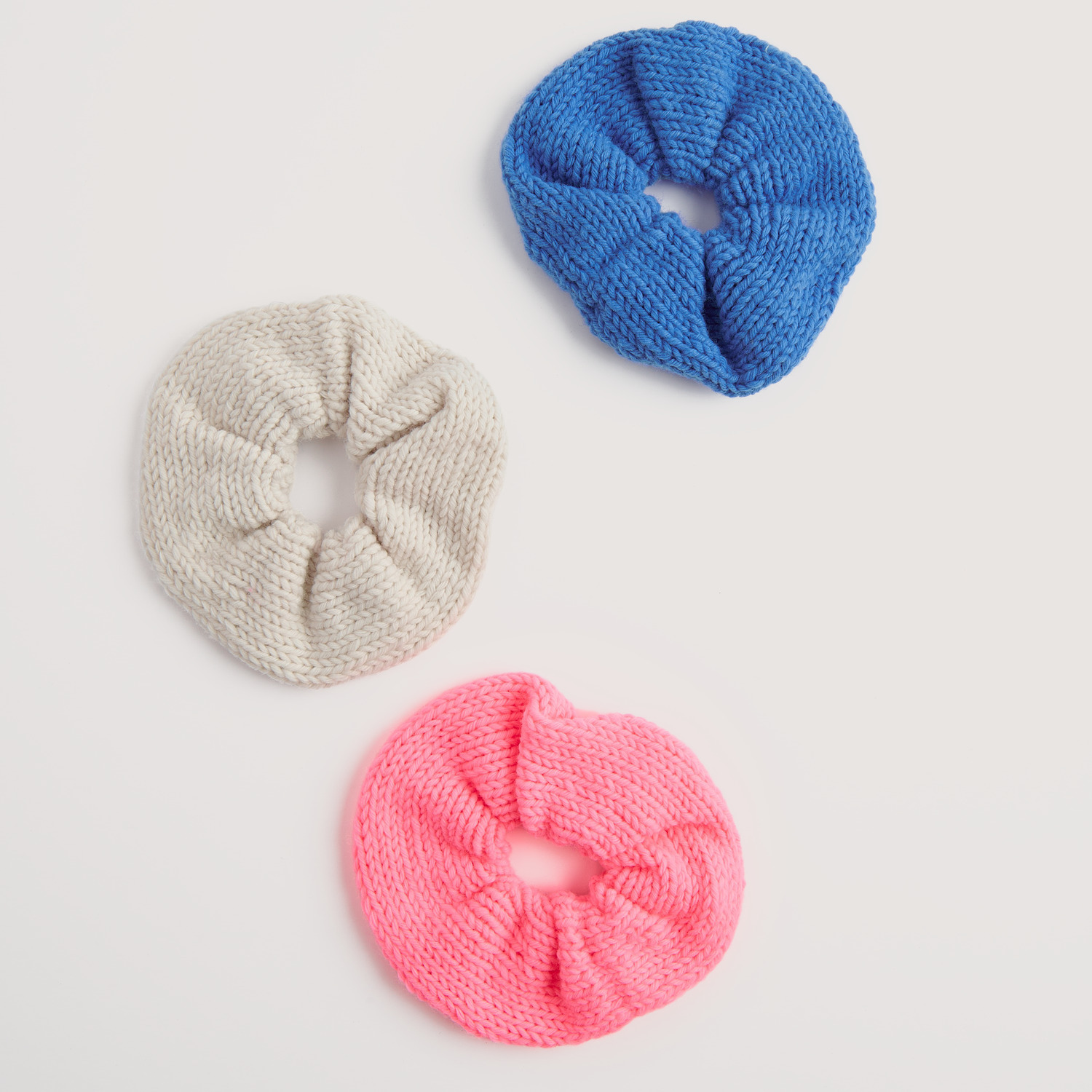 Essentials Vegan Cashmere aran: Drei gestrickte Haargummis in Pink, Blau und Creme auf weißem Hintergrund.