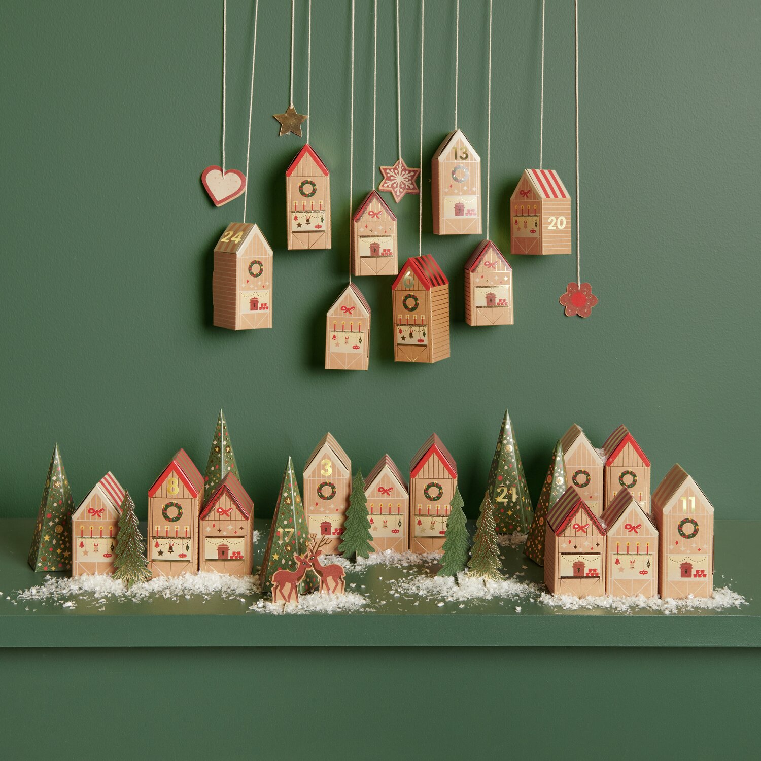 Adventskalender Bastelset: Dekorative Häuschen in Rot und Naturtönen vor grünem Hintergrund.