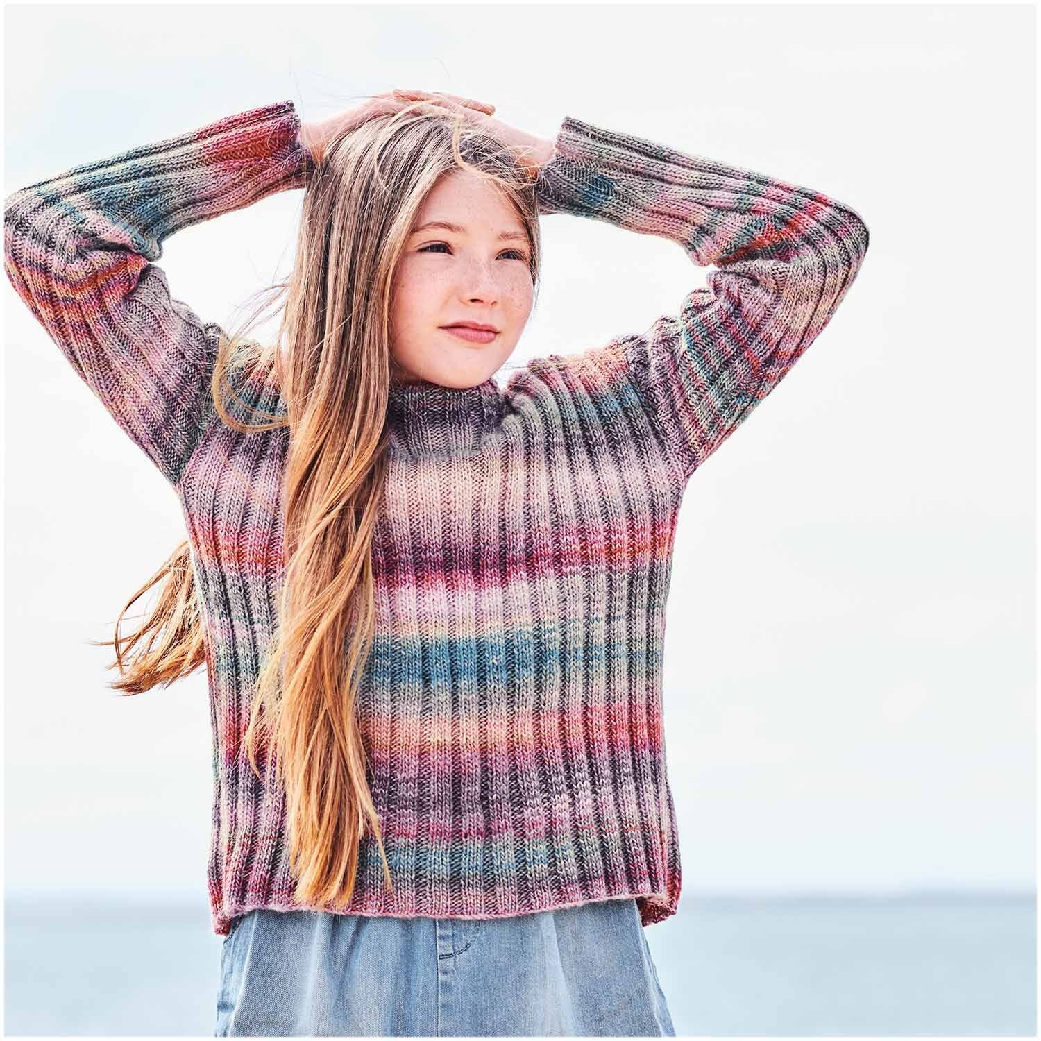 Creative Melange aran Wonderball: Mädchen in gestreiftem Pullover am Strand, gestrickt aus Rico Design Garn.