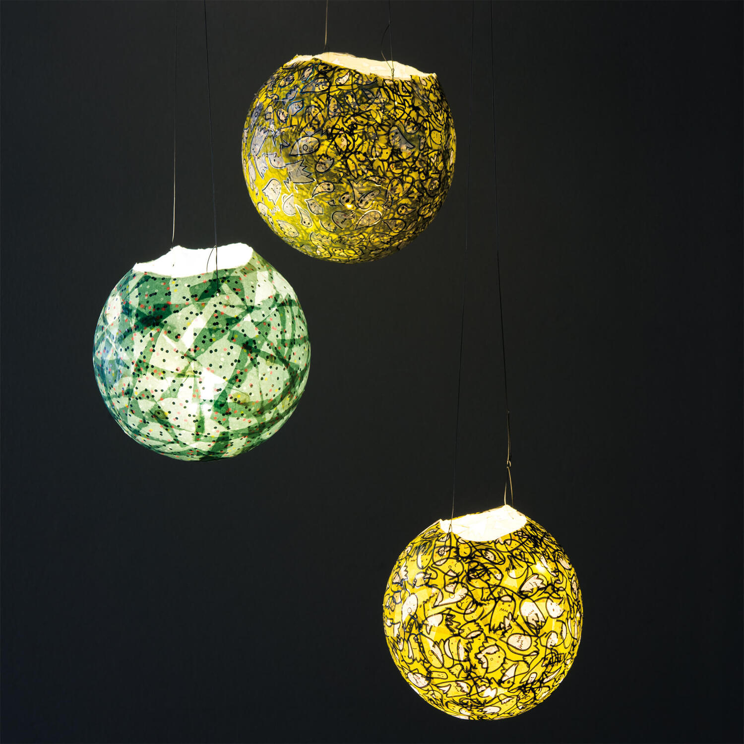 Bastelanleitung Lampion aus Luftballon: Drei bunte, handgefertigte Lampions aus Luftballons hängen vor dunklem Hintergrund.