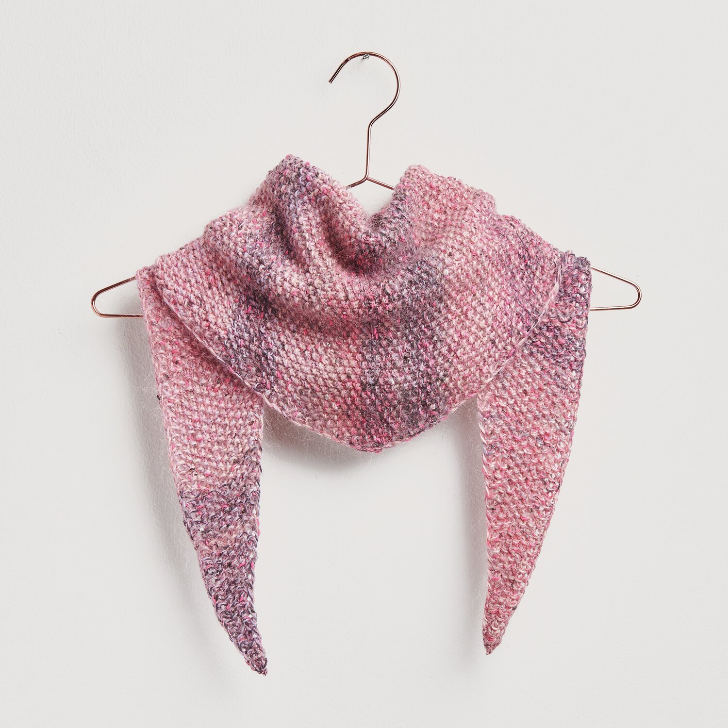 Strickset Dreieckstuch Modell 01b in Beeren- und Pinktönen, aufgehängt an einem Kleiderbügel. Ideal für Frühjahr-Sommer.