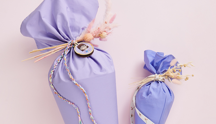 Bastelanleitung Schultüten nähen und besticken: Zwei lila Schultüten mit bunten Bändern und Trockenblumen auf rosa Hintergrund.