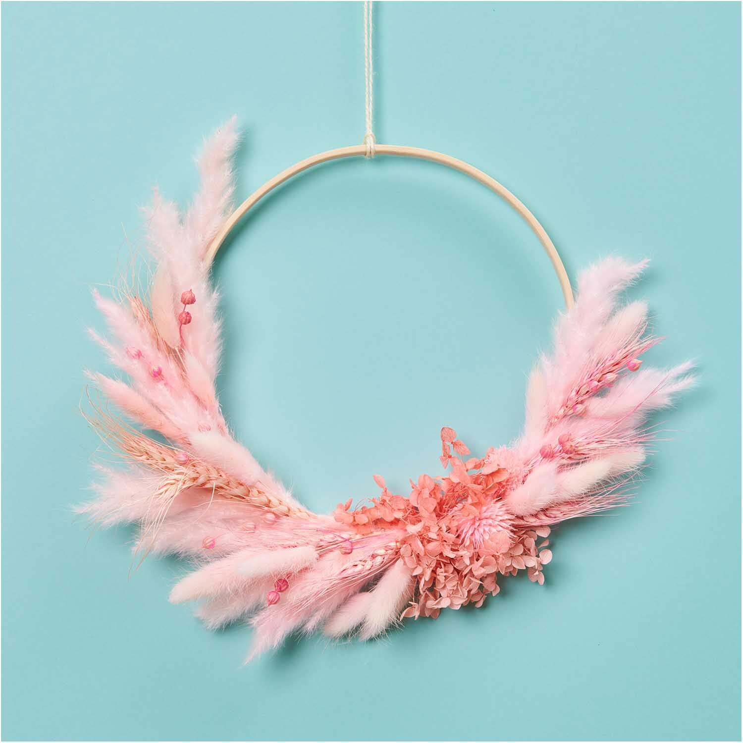 Getrockneter Lagurus pink ca. 40cm 50 Stück von Rico Design: Ein dekorativer Kranz aus rosa Trockenblumen auf hellblauem Hintergrund.
