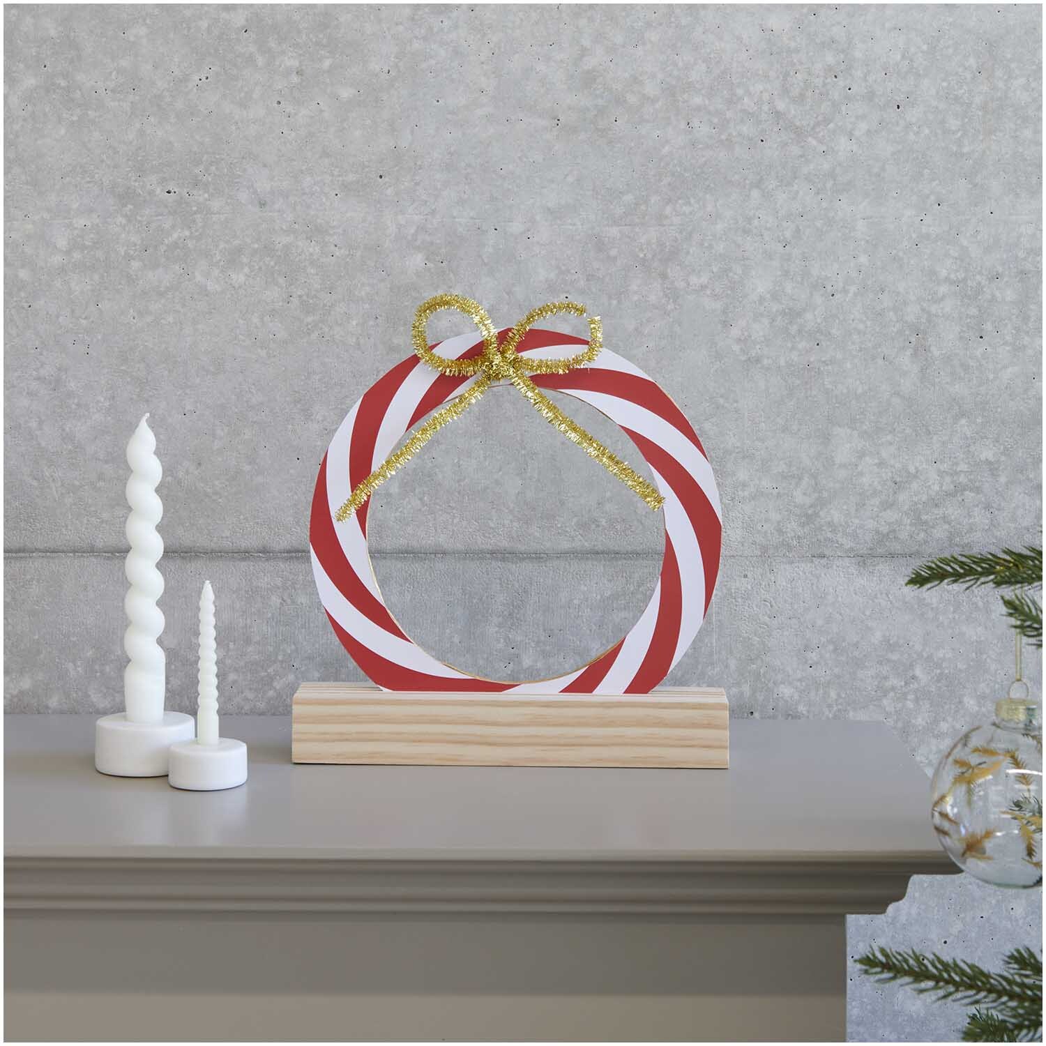 Paper Poetry Kartonring Candy Cane Ø 25cm von Rico Design auf einem Regal mit Kerzen und Dekoration.