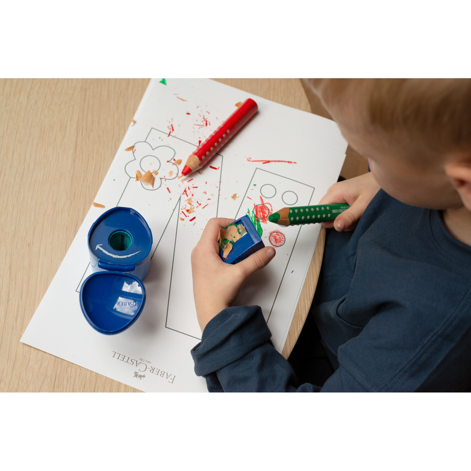 Buntstift Grippy Set + Spitzer: Kind malt mit roten und grünen Stiften auf Papier, blaue Spitzdose.