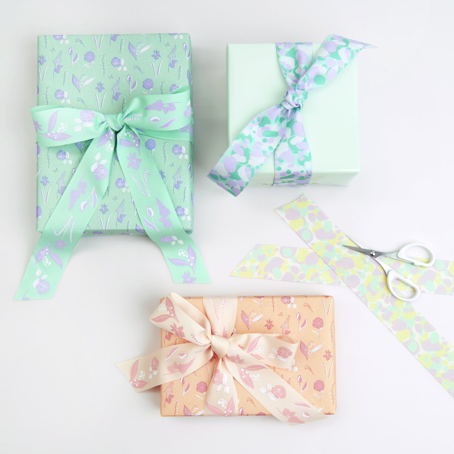 Paper Poetry Taftband Blumenwiese: Zwei Geschenke mit floralen Bändern in Pastellfarben, Schere daneben.
