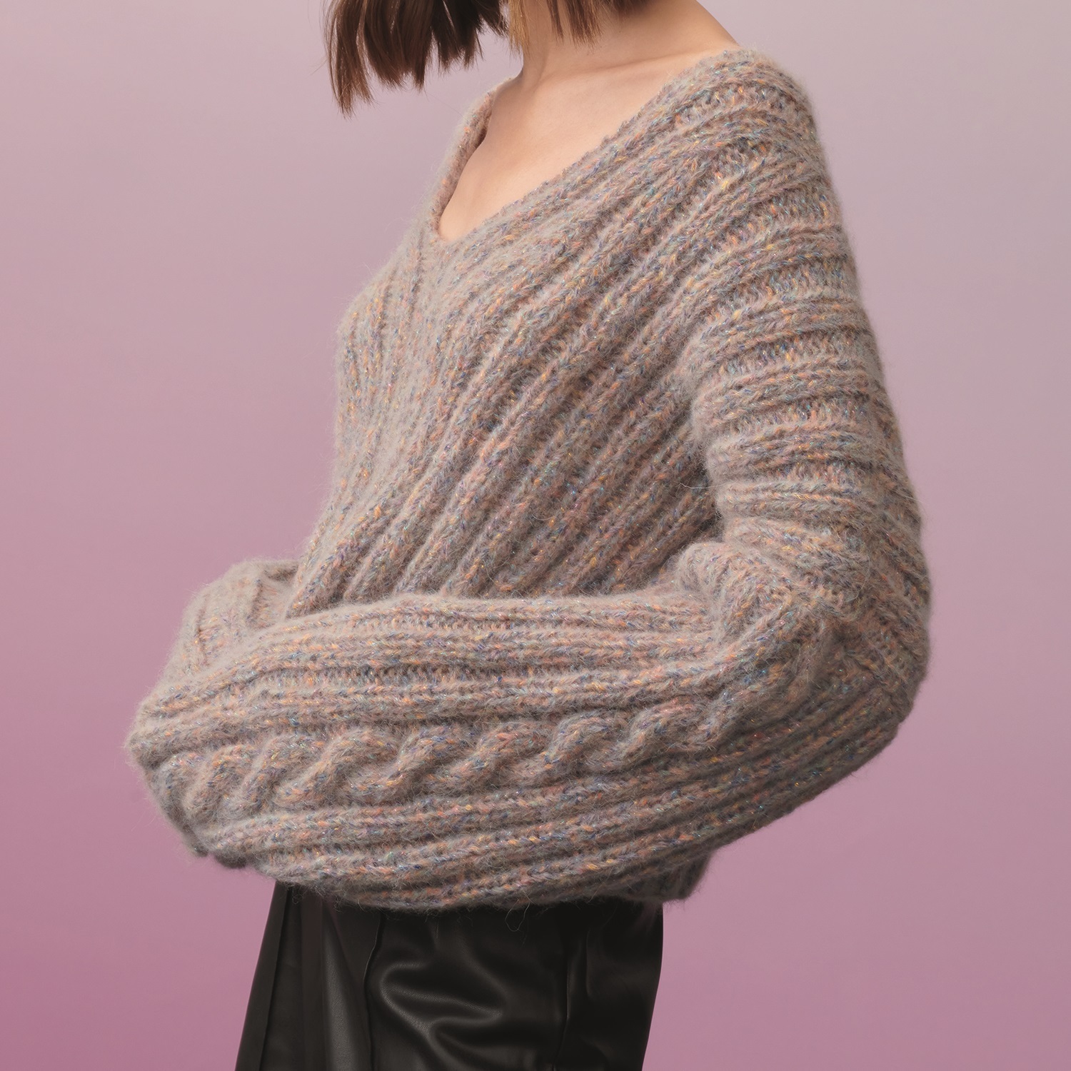 Strickanleitung Pullover aus Fashion Alpaca Bling Bling: Frau trägt grob gestrickten Pullover in Beige mit Zopfmuster vor lila Hintergrund.