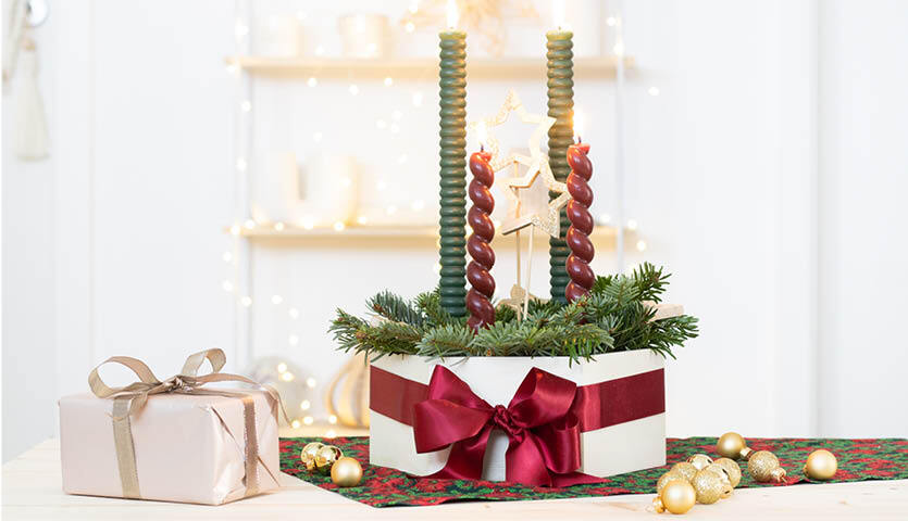 Bastelanleitung Adventskranz by machsschoen: Ein festlicher Adventskranz mit grünen Zweigen, roten und grünen Kerzen, dekoriert mit einer roten Schleife.