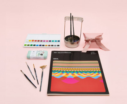 Ein Aquarellblock mit Aquarellfarbkasten, Pinseln und Pinselwascher. Fotosetting rosa Hintergrund.