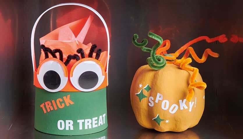 Anleitung Halloween-Kürbisse und -Körbchen: Orange Kürbis-Deko mit grünen Details und ein grünes Körbchen mit Augen und Schriftzug.