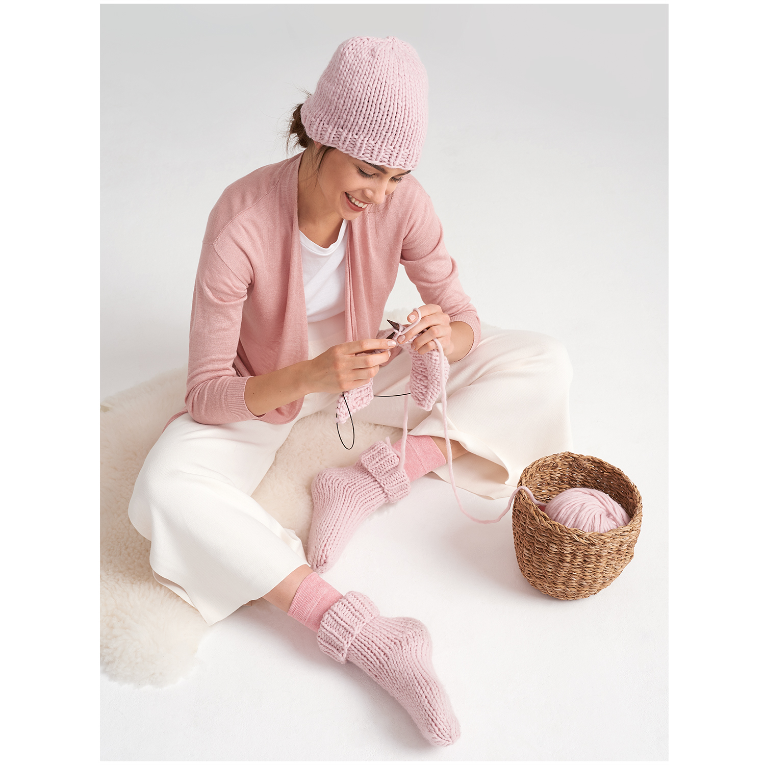 Essentials Super super chunky: Frau strickt mit rosa Wolle, trägt passende Mütze und Socken.