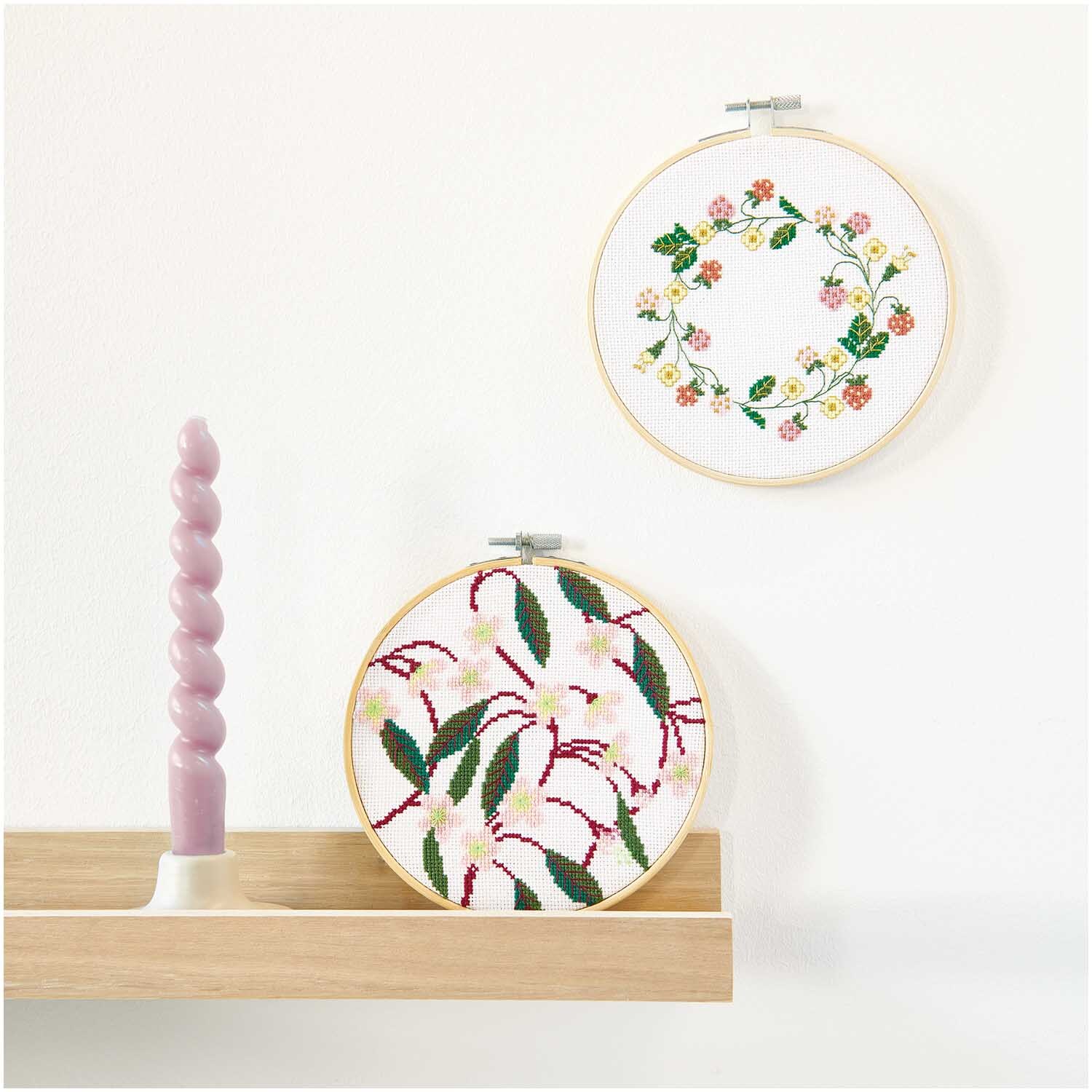 Stickpackung Bild Kirschblüten zeigt zwei runde Stickrahmen mit floralen Designs an einer Wand.
