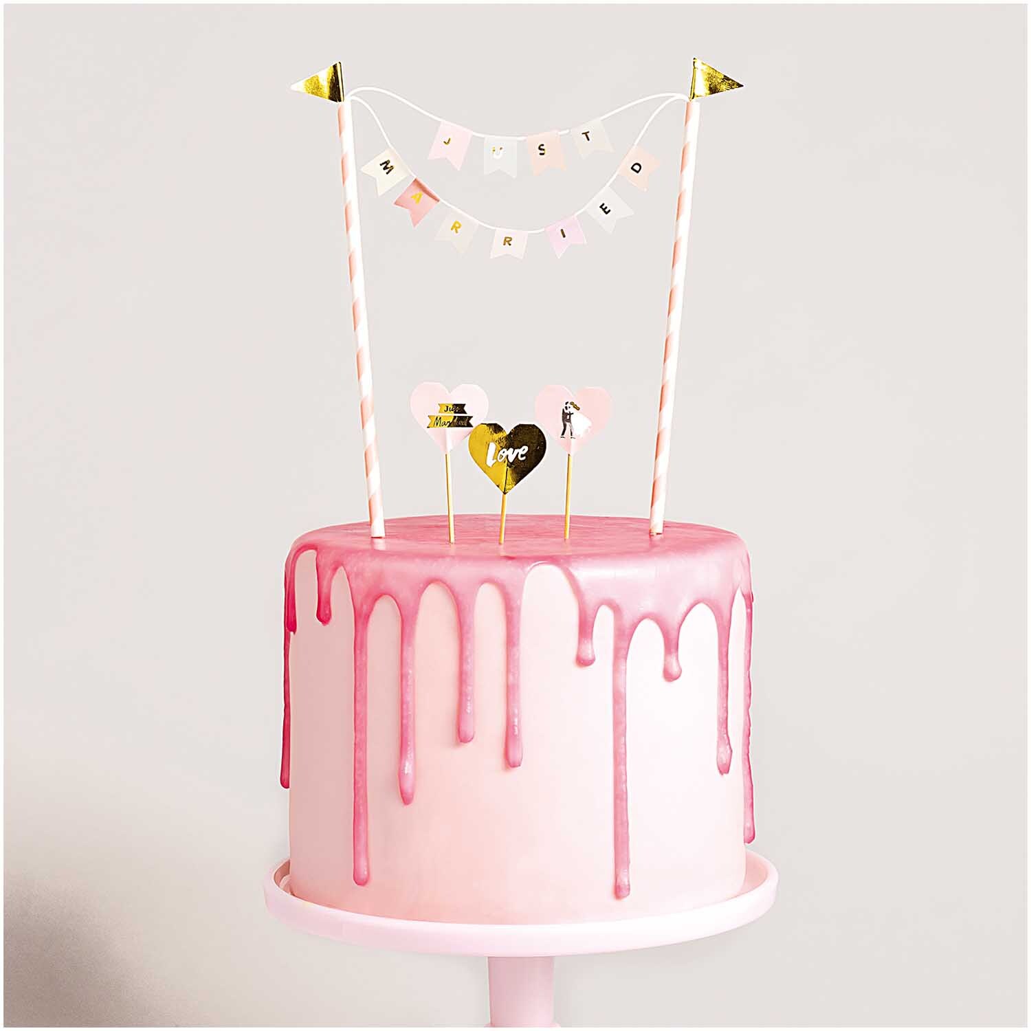 Kuchendekoration Just Married: Rosa Torte mit tropfendem Zuckerguss und dekorativen Bannern von Rico Design.