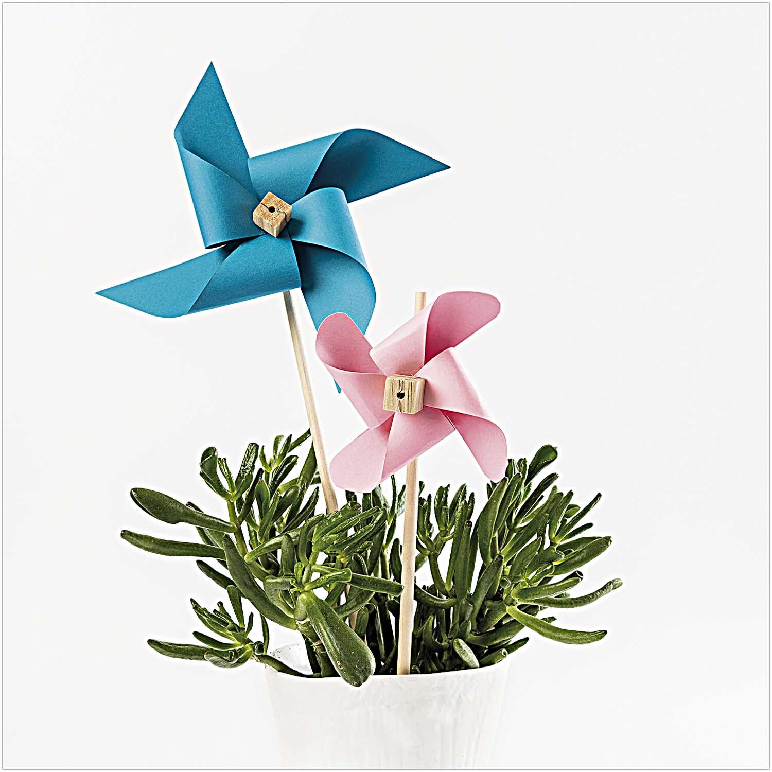 DIY-Holzbastelset: Zwei bunte Windräder in Blau und Rosa stecken in einem Topf mit grünen Pflanzen.
