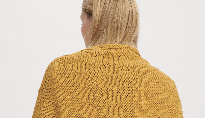 Strickanleitung Poncho aus Classik: Frau trägt gelben, gestrickten Poncho mit geometrischem Muster.