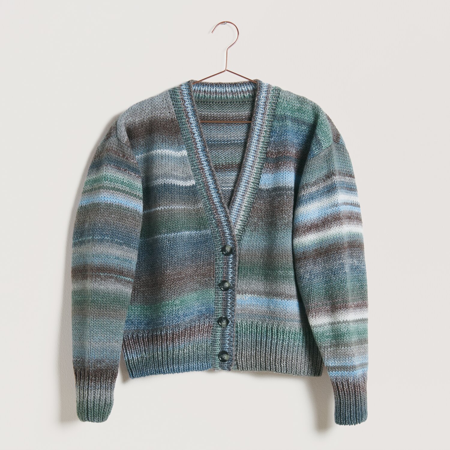 Strickset Jacke Modell 25 aus Die Neue Masche No. 10, gestrickt in Blau- und Brauntönen, auf einem Kleiderbügel vor neutralem Hintergrund.