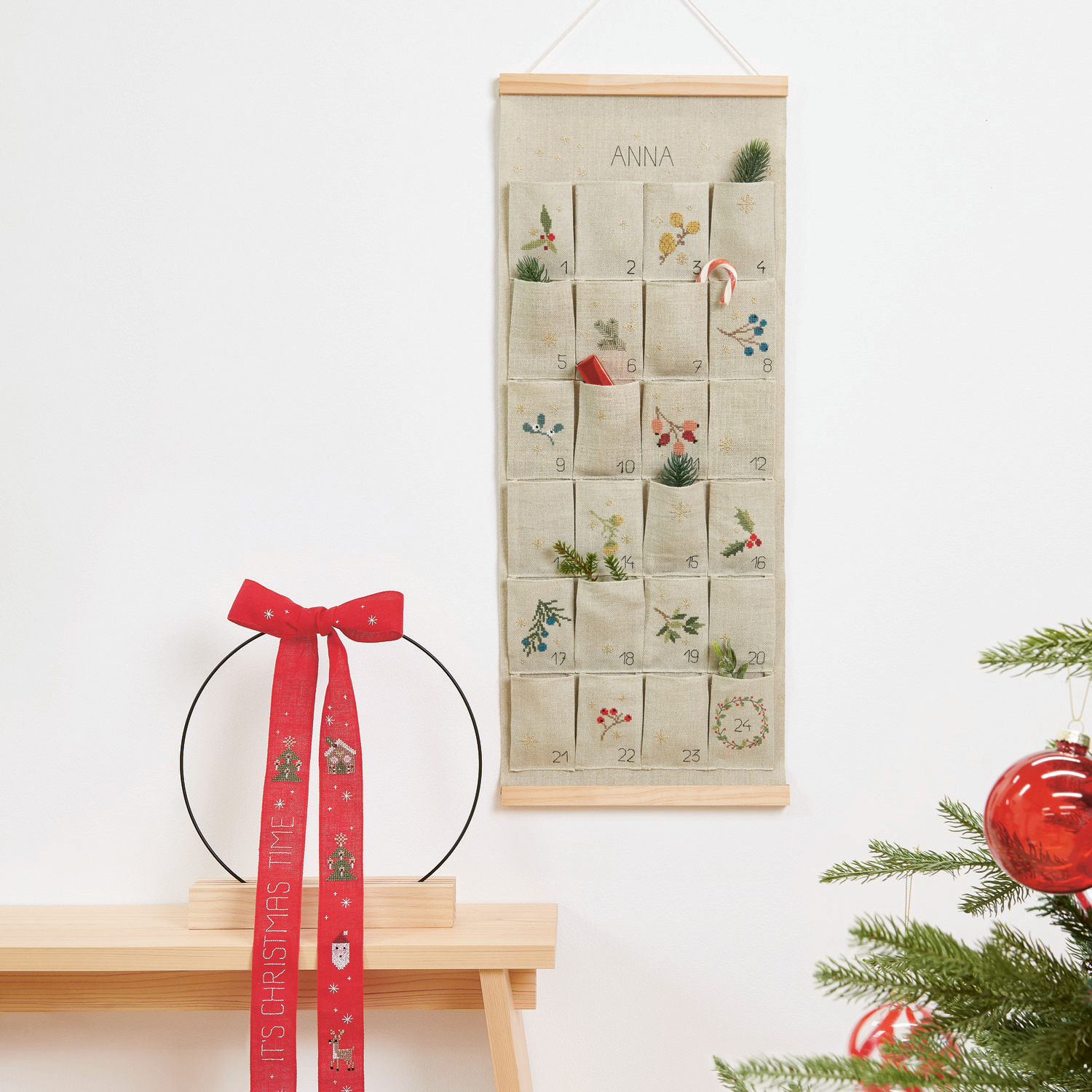 Stickbuch Put a Bow on It Nr. 185: Adventskalender mit Taschen und roter Schleife, dekoriert mit weihnachtlichen Motiven.
