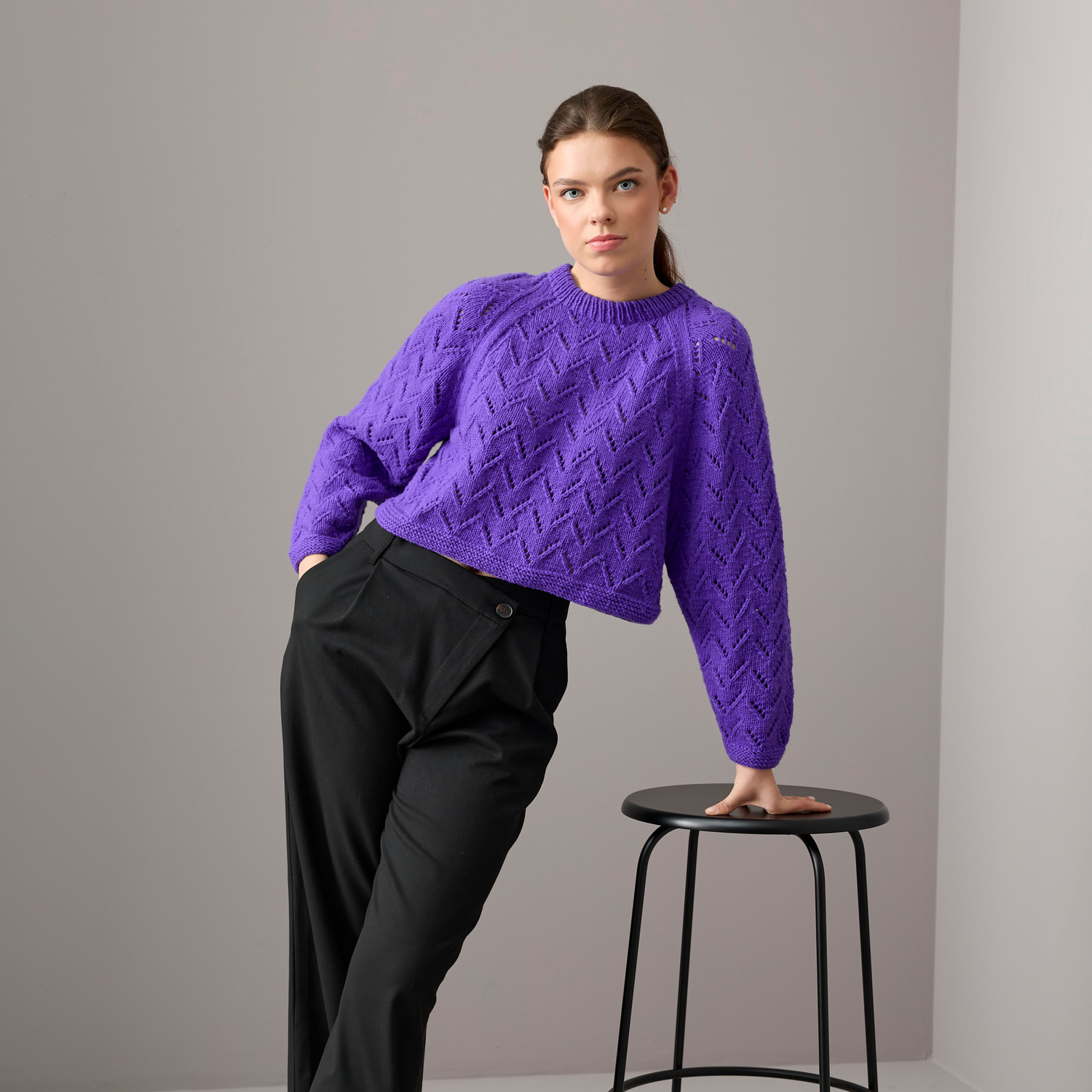 Special "Vegan Cashmere" Pullover in Violett von Rico Design, getragen von einer Frau, die an einem Hocker lehnt.