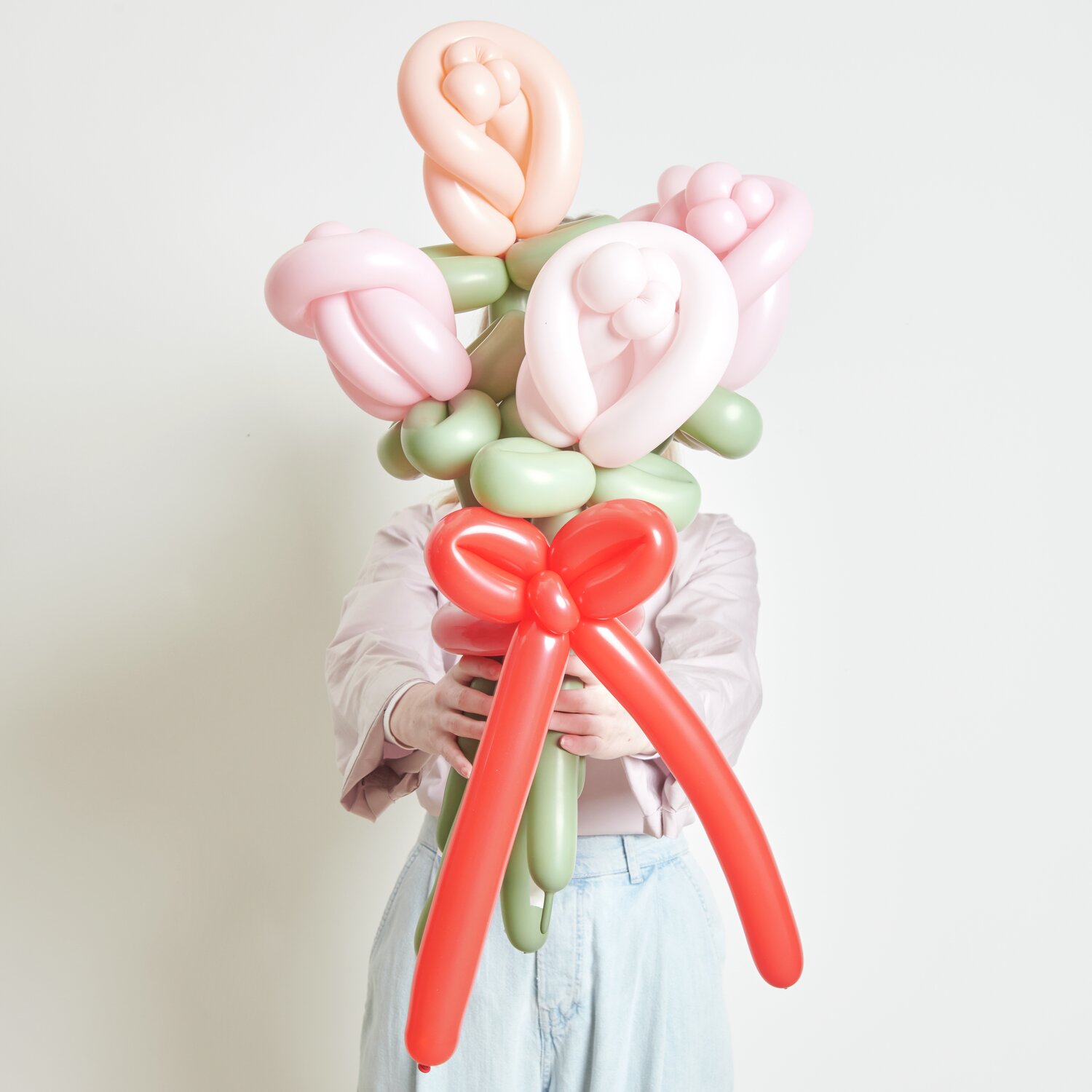Ballonstrauß Rosen Rosa Mix: Ein Strauß aus rosa und grünen Ballons, kunstvoll gebunden, mit roter Schleife.
