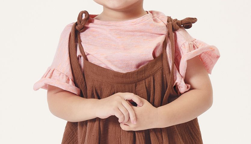 Nähanleitung Latzhose aus Krinkelmusselin: Kind in brauner Latzhose und rosa Shirt mit Rüschenärmeln.
