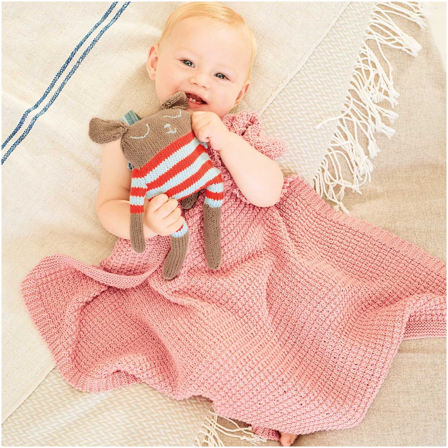 Baby Organic Cotton: Ein Baby in altrosa Decke von Rico Design hält ein gestricktes Stofftier.