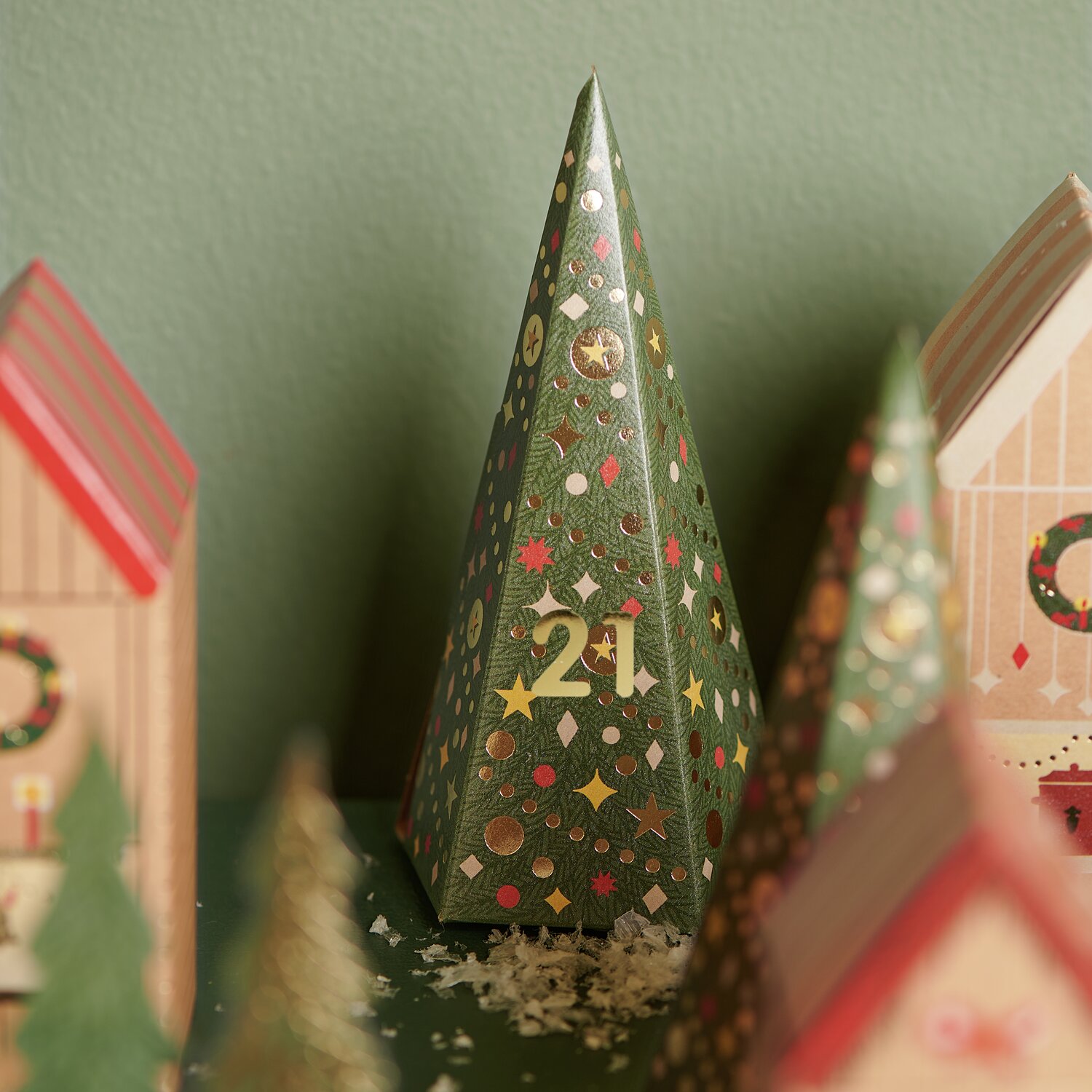 Adventskalender Bastelset: Grüner Tannenbaum mit goldenen Zahlen und bunten Mustern, umgeben von kleinen Häuschen.