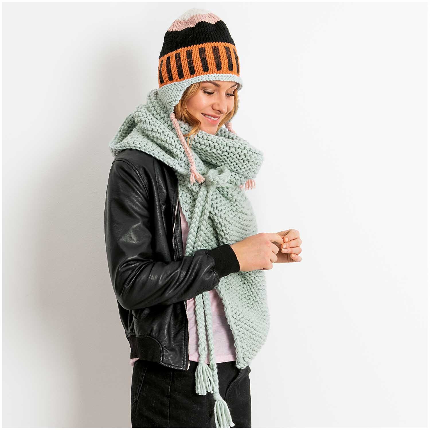 Essentials Mega Wool chunky: Frau mit gestricktem Schal und Mütze in Orange von Rico Design.