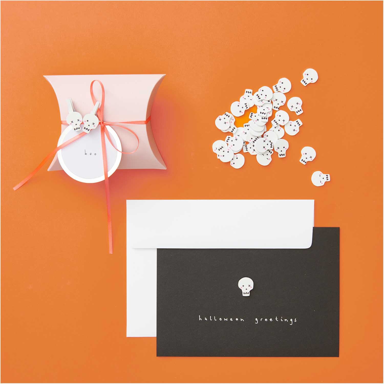 Holzclips Totenkopf Mix weiß 8 Stück von Rico Design auf orangefarbenem Hintergrund mit Geschenkbox und Grußkarte.