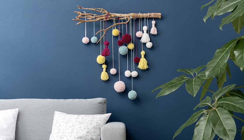 Bastelanleitung für einen Wandbehang zeigt bunte Pompons und Tasseln in verschiedenen Farben. Ideal für kreative Dekorationen.