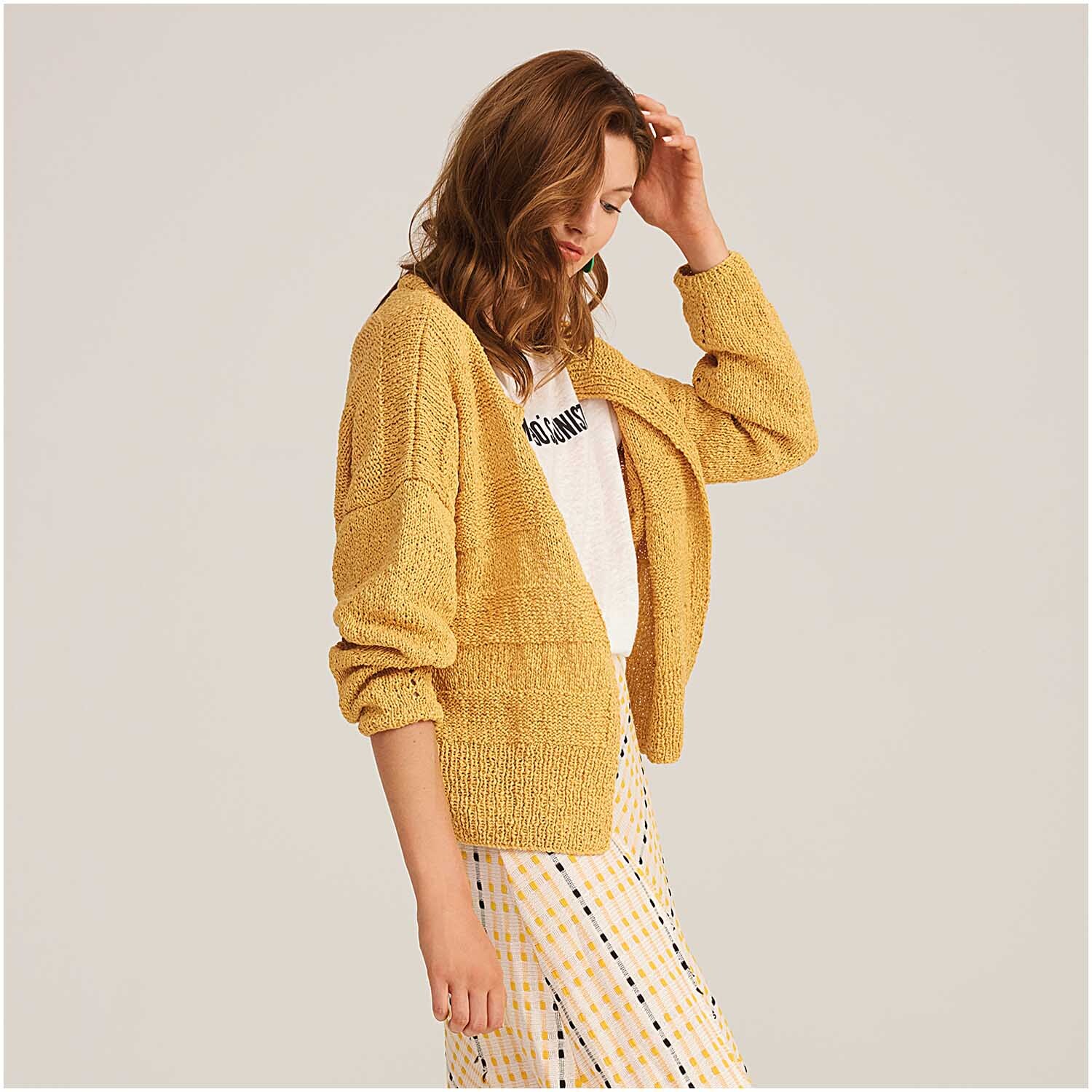 Fashion Linen Swell aran: Frau trägt senfgelbe Strickjacke von Rico Design, kombiniert mit gestreiftem Rock.