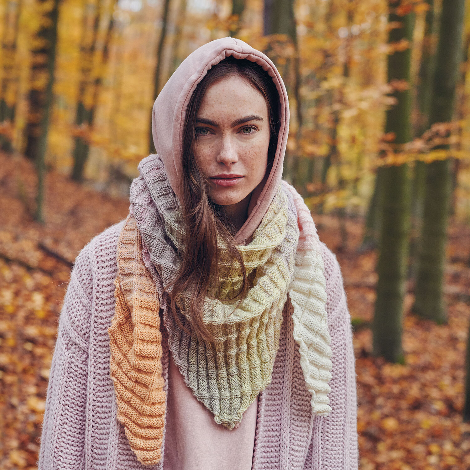 Eine Frau trägt eine gestrickte Jacke aus rosa Garn und dazu einen gestrickten Dreiecksschal aus einem Farbverlaufsgarn.