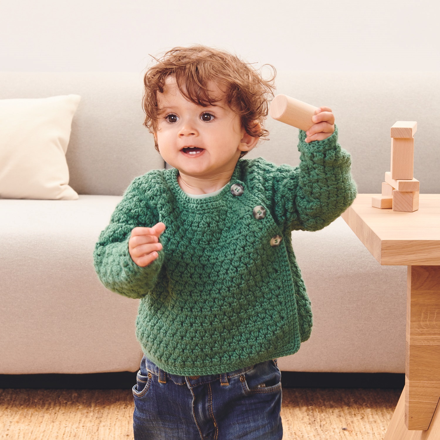 Häkelanleitung Jacke aus Baby Dream dk Uni: Kind trägt gestrickte Jacke, spielt mit Bauklötzen im Wohnzimmer.